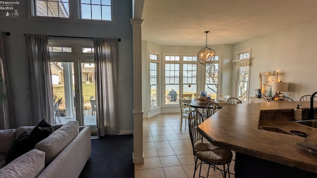 interior space with ornate columns, a kitchen bar, pendant lighting, a notable chandelier, and light tile patterned flooring