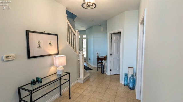 hallway featuring light tile patterned flooring, baseboards, and stairs