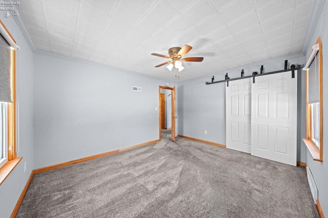 unfurnished bedroom with a barn door, visible vents, baseboards, carpet, and crown molding