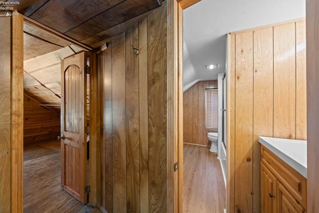 hallway with vaulted ceiling, light wood-type flooring, and wooden walls