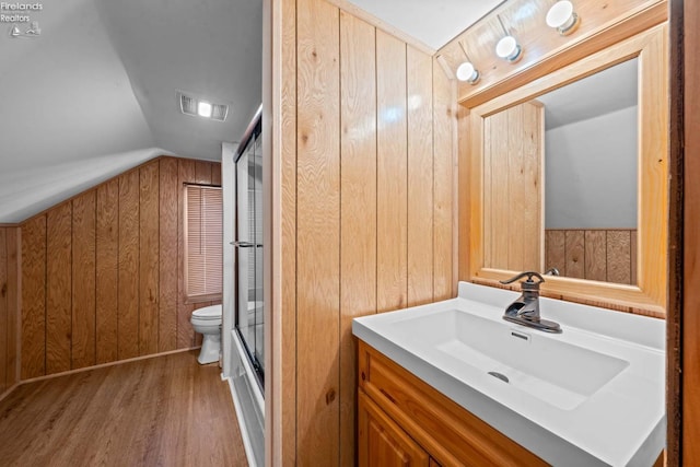 full bathroom featuring wooden walls, lofted ceiling, toilet, wood finished floors, and vanity