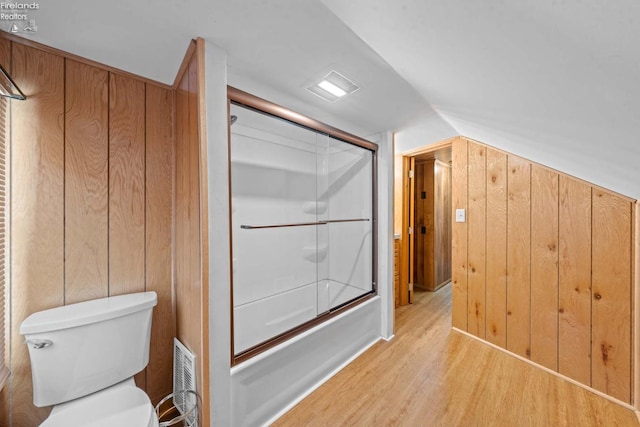 bathroom with combined bath / shower with glass door, wood walls, toilet, and wood finished floors