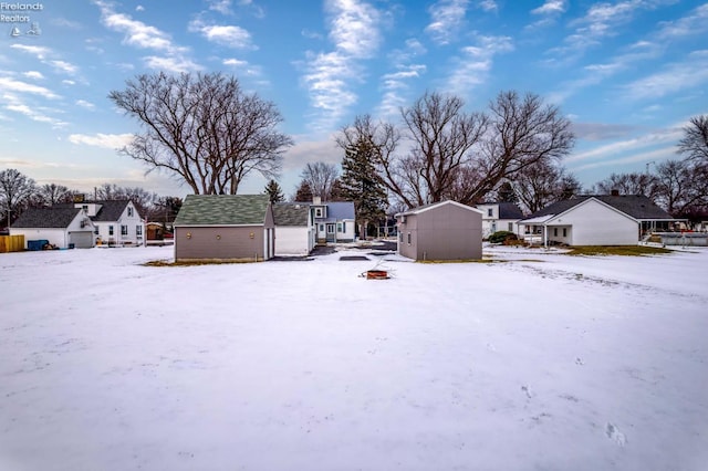 snowy yard featuring an outbuilding, a storage unit, and a residential view