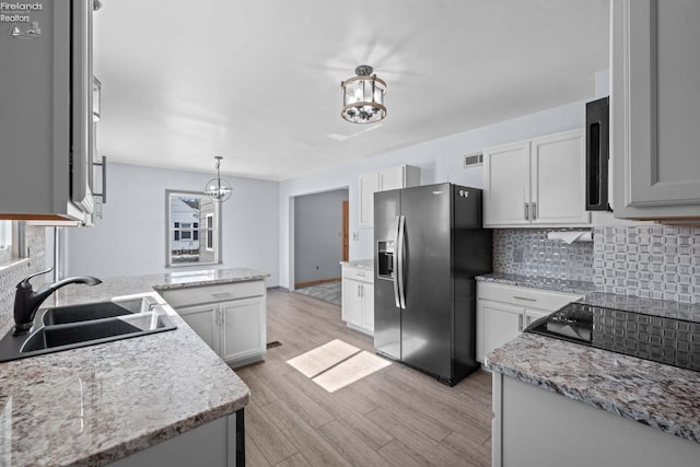 kitchen with stainless steel refrigerator with ice dispenser, hanging light fixtures, backsplash, white cabinets, and a sink