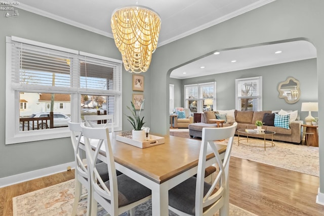 dining room featuring an inviting chandelier, crown molding, arched walkways, and wood finished floors