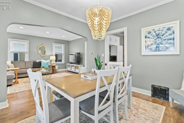 dining area with arched walkways, crown molding, wood finished floors, a chandelier, and baseboards