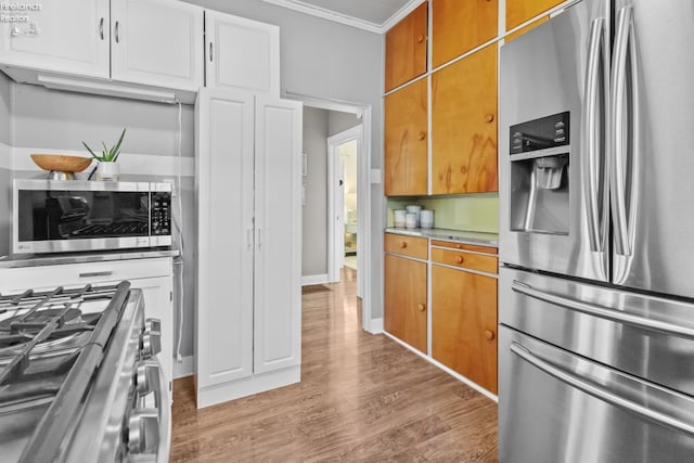 kitchen with crown molding, stainless steel appliances, light countertops, brown cabinetry, and light wood-type flooring