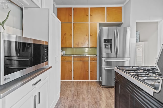 kitchen with light wood-style floors, ornamental molding, and stainless steel appliances