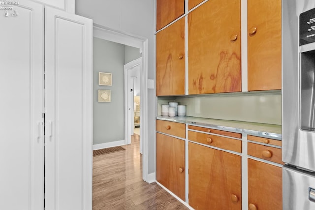 kitchen with light countertops, brown cabinetry, wood finished floors, stainless steel fridge, and baseboards