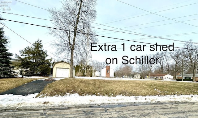 community sign featuring aphalt driveway, a yard, and a detached garage