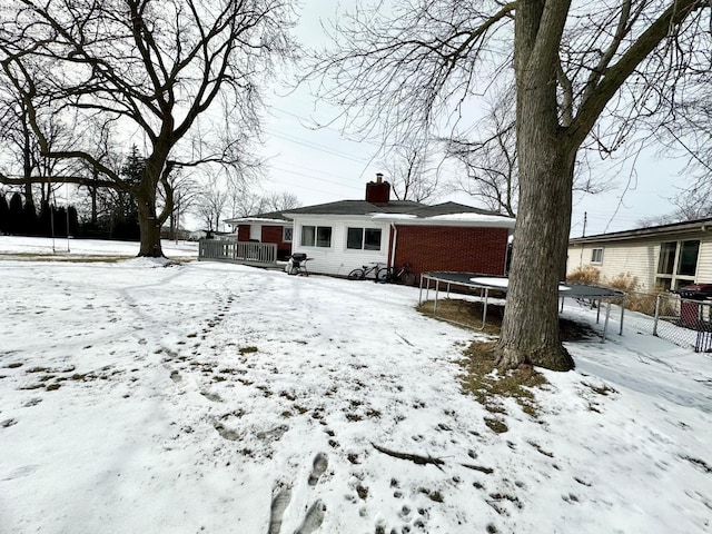 snow covered house with a garage, brick siding, a trampoline, and a chimney