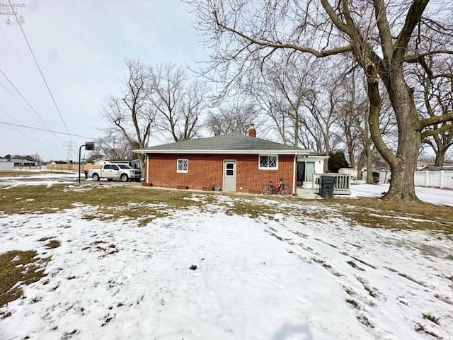 snow covered rear of property featuring brick siding and a chimney