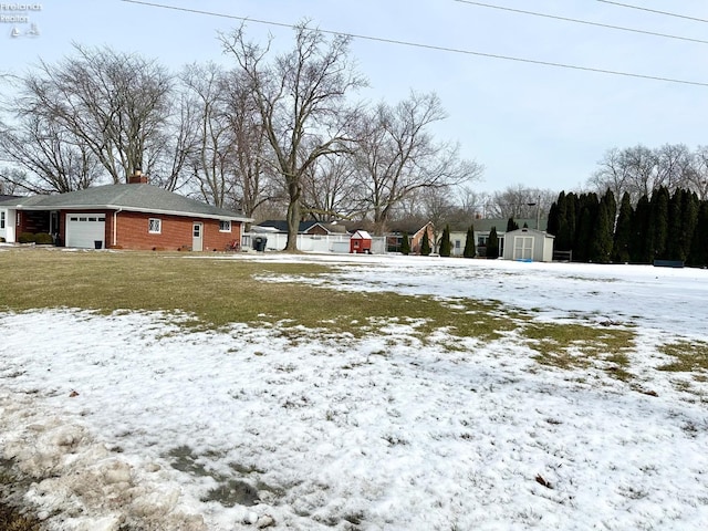 yard layered in snow with an outbuilding, an attached garage, and a shed