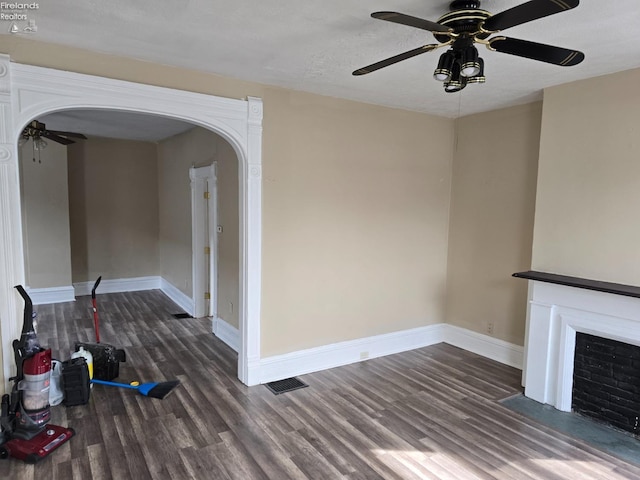 unfurnished living room featuring baseboards, a fireplace with flush hearth, arched walkways, and dark wood-type flooring