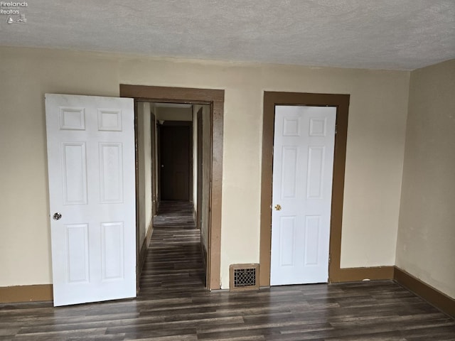 spare room featuring dark wood-style floors, baseboards, visible vents, and a textured ceiling