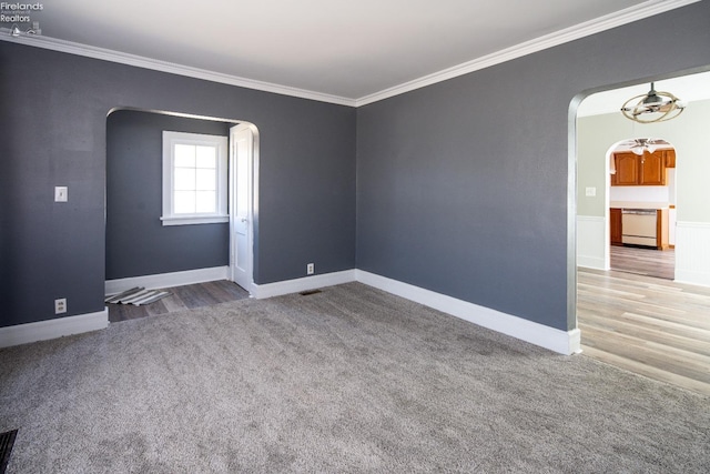 carpeted spare room with arched walkways, visible vents, crown molding, and baseboards