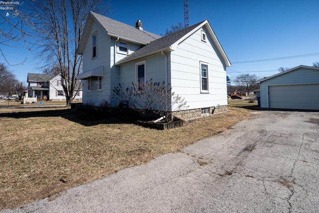 view of side of home with an outbuilding, a shingled roof, a lawn, and a detached garage