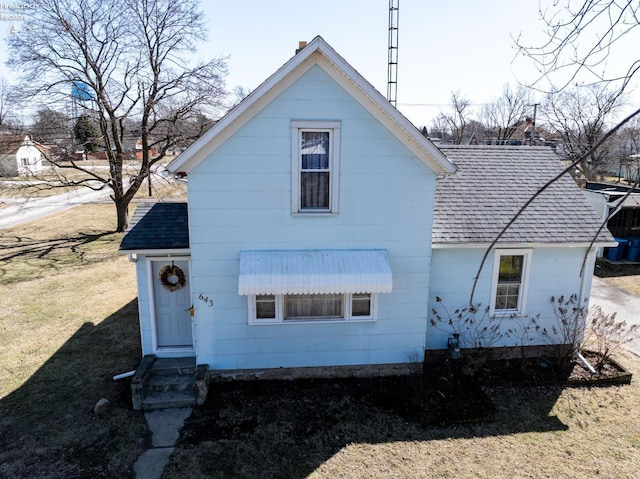 rear view of property with entry steps, a shingled roof, and a lawn