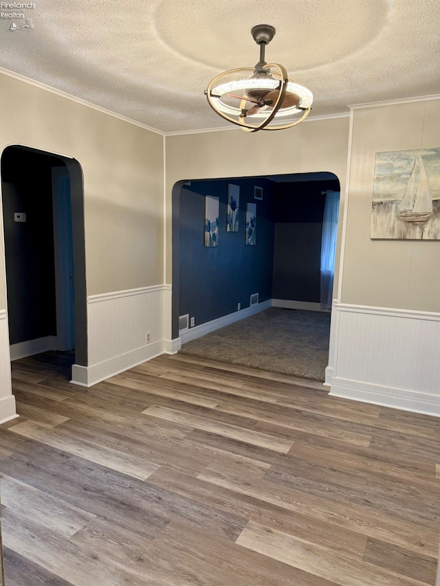 unfurnished dining area featuring arched walkways, wood finished floors, and crown molding