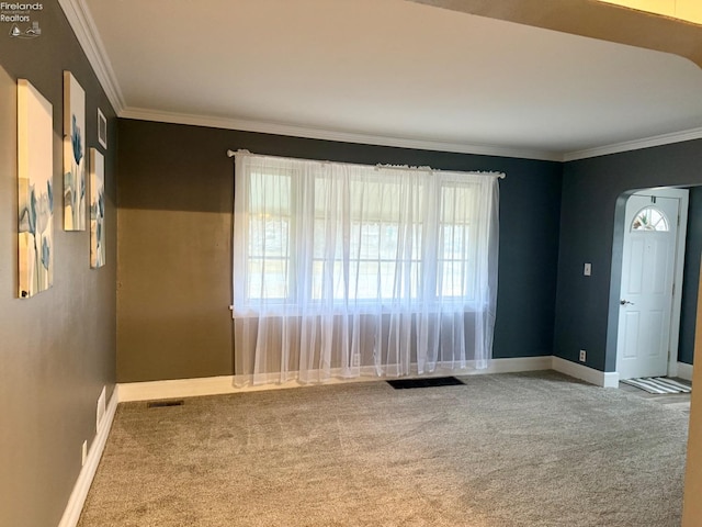 carpeted empty room with ornamental molding, arched walkways, and baseboards