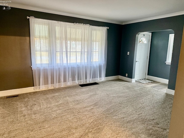 spare room featuring visible vents, arched walkways, baseboards, carpet, and crown molding