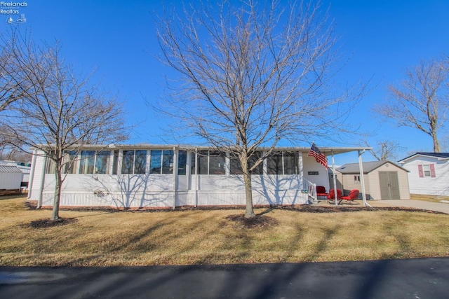 view of front of house featuring a storage unit, a front yard, and a sunroom