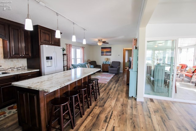 kitchen with a breakfast bar, dark wood finished floors, open floor plan, dark brown cabinets, and white fridge with ice dispenser