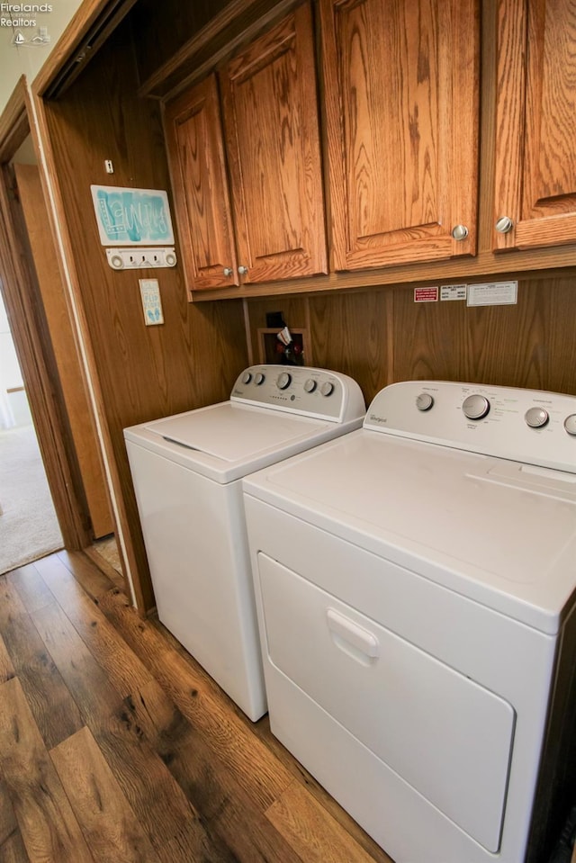 washroom featuring dark wood-style floors, cabinet space, wooden walls, and washing machine and clothes dryer