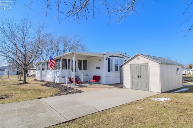 manufactured / mobile home with an outbuilding, a sunroom, driveway, a shed, and a front yard