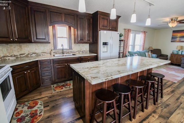 kitchen with white appliances, a kitchen island, a breakfast bar area, open floor plan, and a sink