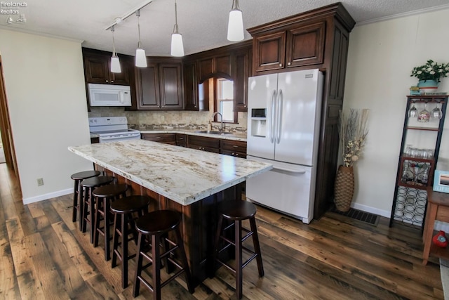 kitchen with dark wood-type flooring, white appliances, a kitchen island, a sink, and pendant lighting