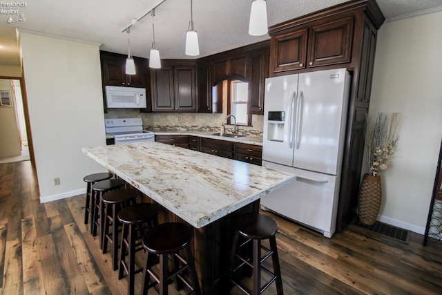 kitchen featuring white appliances, dark wood finished floors, decorative light fixtures, a center island, and a sink