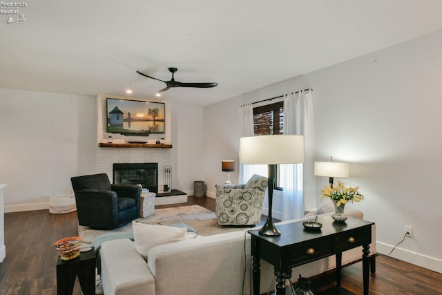 living area featuring a ceiling fan, a brick fireplace, baseboards, and wood finished floors