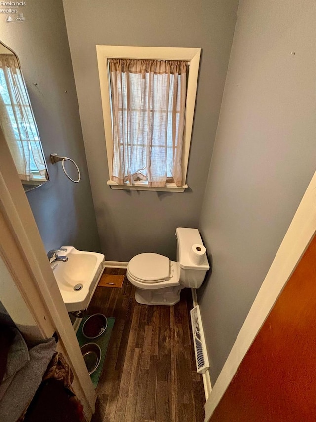 half bath featuring visible vents, baseboards, toilet, wood finished floors, and a sink