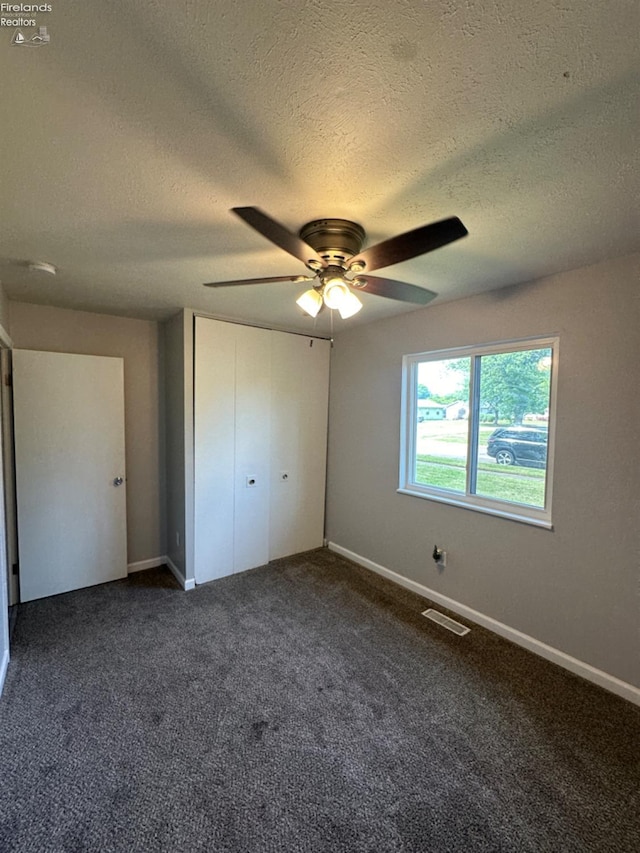 unfurnished bedroom with baseboards, visible vents, ceiling fan, dark carpet, and a closet