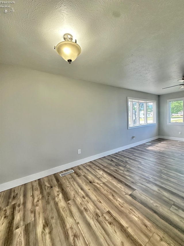 empty room featuring a textured ceiling, wood finished floors, a ceiling fan, visible vents, and baseboards