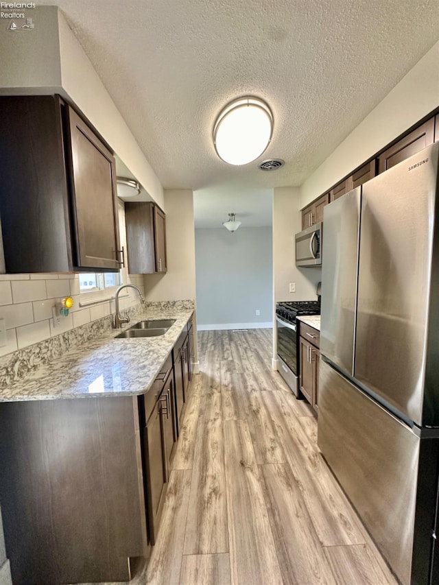 kitchen featuring dark brown cabinetry, visible vents, light stone countertops, stainless steel appliances, and a sink