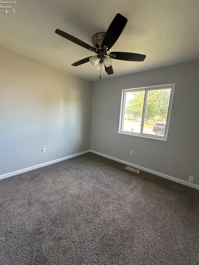 empty room with a textured ceiling, a ceiling fan, visible vents, baseboards, and dark colored carpet