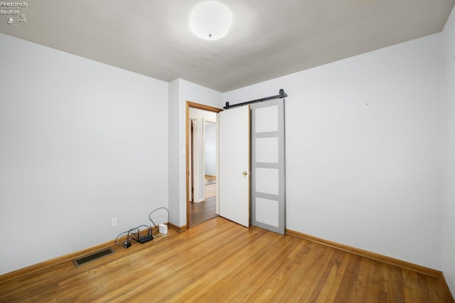 empty room with light wood finished floors, a barn door, visible vents, and baseboards