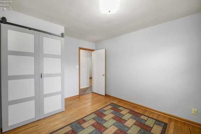 unfurnished bedroom with a barn door, baseboards, light wood-style flooring, and a closet