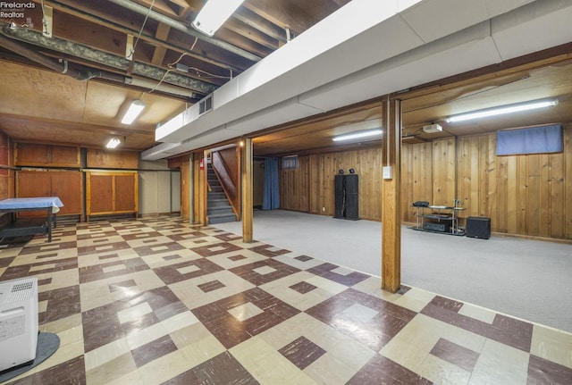 finished basement with stairway, wooden walls, visible vents, and tile patterned floors