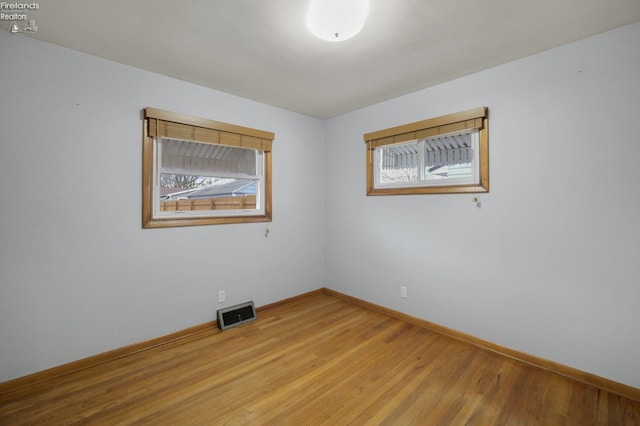 empty room featuring light wood finished floors, visible vents, and baseboards