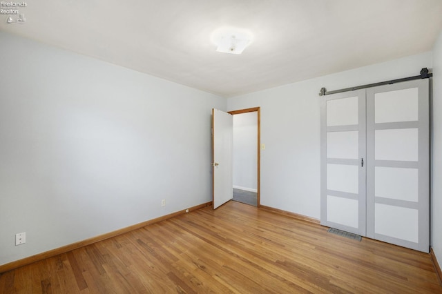 unfurnished room featuring light wood-style floors, visible vents, baseboards, and a barn door