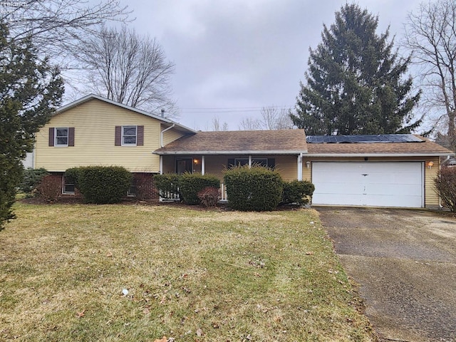 split level home with aphalt driveway, a front yard, a garage, and solar panels