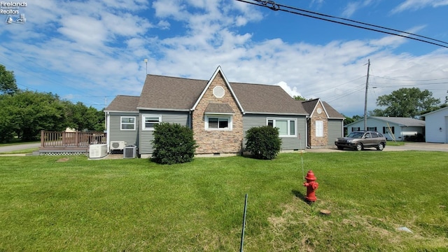 view of front of property with a deck, roof with shingles, a front yard, and central air condition unit