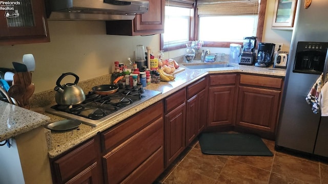 kitchen featuring stainless steel appliances, dark tile patterned floors, a sink, light stone countertops, and wall chimney exhaust hood