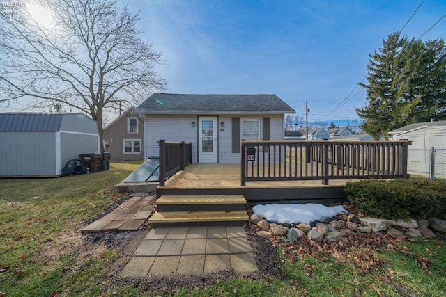 back of property with a storage shed, roof with shingles, an outbuilding, a yard, and a wooden deck