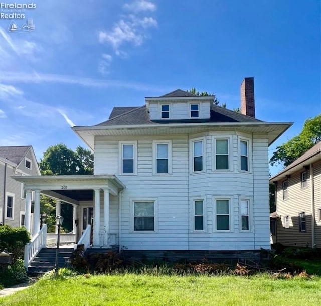 back of property with covered porch, a chimney, and a yard