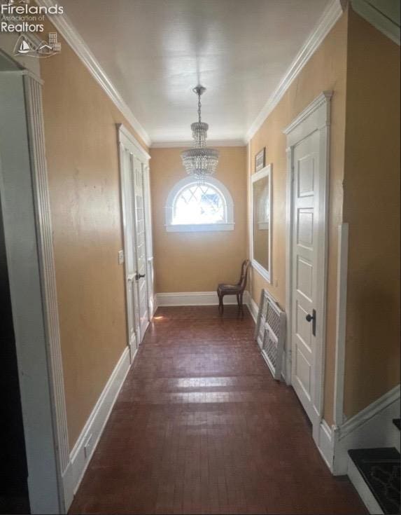 entryway featuring ornamental molding, dark wood-type flooring, a notable chandelier, and baseboards