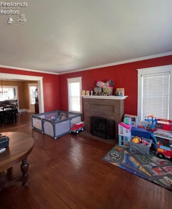 living area featuring a brick fireplace, ornamental molding, and wood finished floors